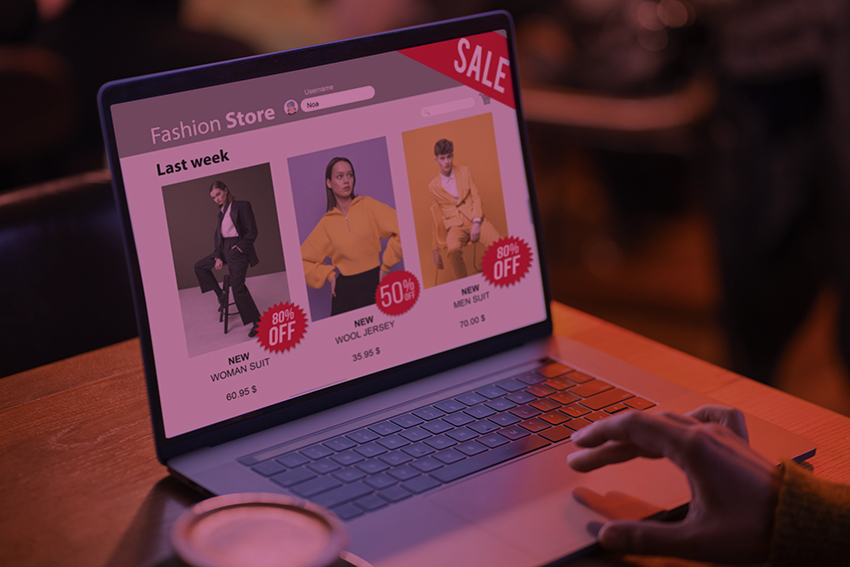 Laptop aberto com um e-commerce sendo exibido na tela. A mão de uma pessoa usando o laptop aparece.