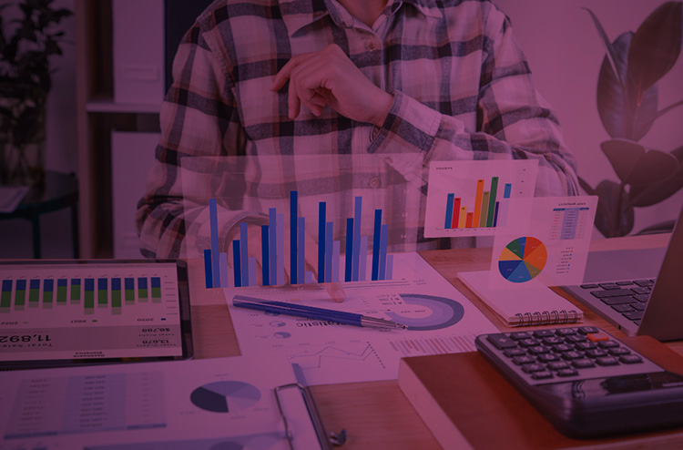 Homem analisando dados em uma folha. Seu rosto não aparece, somente o tronco e as mãos sobre uma mesa. Alguns desses charts aparecem pela imagem como projeções virtuais.